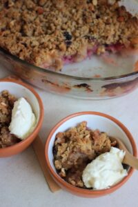 Two tiny bowls with apple crumble and a scoop of whipped cream.