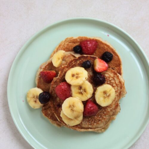 Banana pancakes with banana slices, strawberries, and blueberries on an aqua green plate.