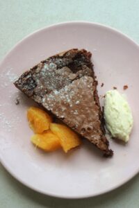 A portion of chocolate cake with oranges slices and whipped cream on a plate.