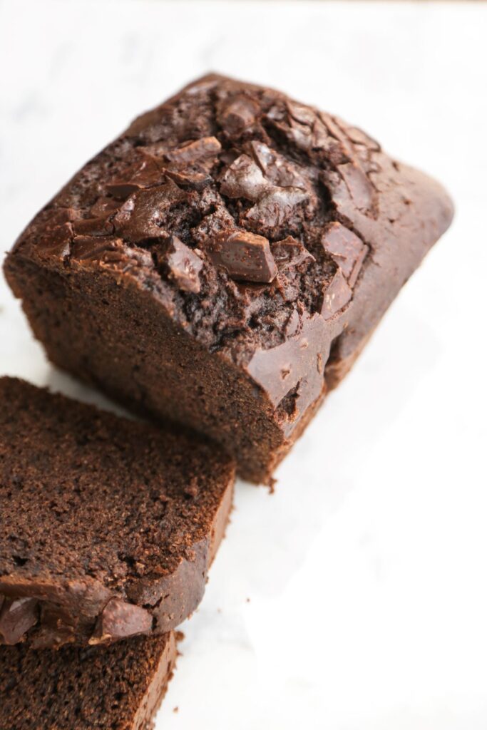 A gluten free chocolate loaf cake and a slice of it on a white surface.