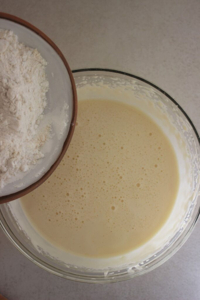 Plate with flour is about to be poured into a glass bowl with a white liquid.