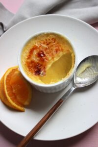 Ramekin with creme brulee without a piece. A spoon with rest of the creme brulee.
