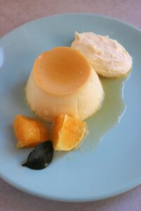 Individual flan with orange slices and whipped cream on a light blue plate.