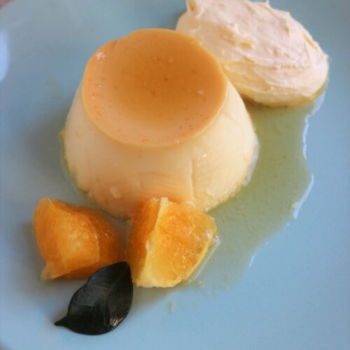 Individual flan with orange slices and whipped cream on a light blue plate.