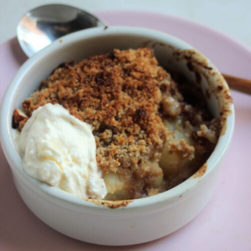 White ramekin with pear crumble and a scoop of whipped cream.