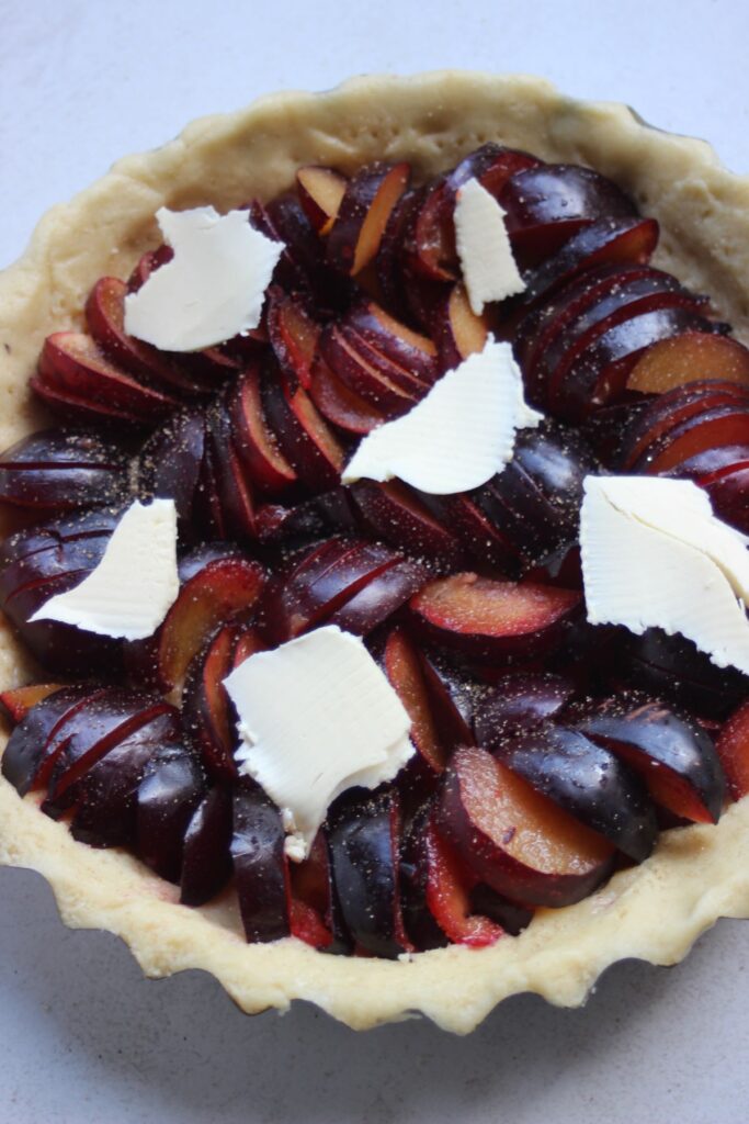 Plum tart raw with pieces of butter on the top.