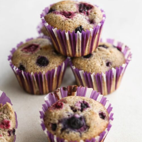 Four mixed berry and lemon muffins with liners on a white surface.