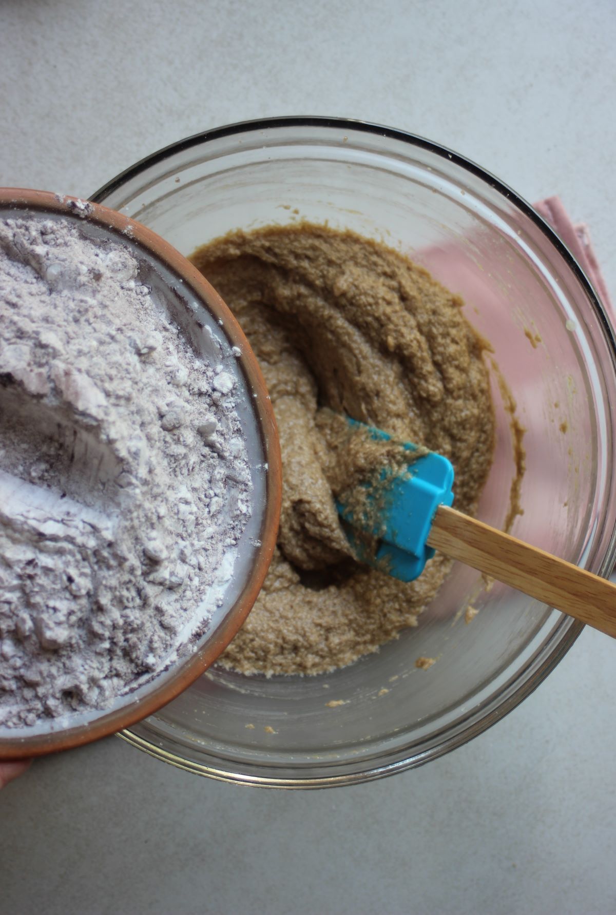Plate with flour is about to be poured into a glass bowl with a mixture and a rubber spatula.