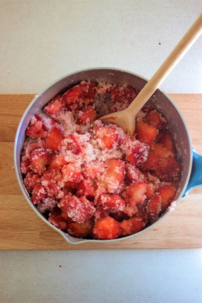 A saucepan with chopped strawberries and sugar, and a wooden spoon..