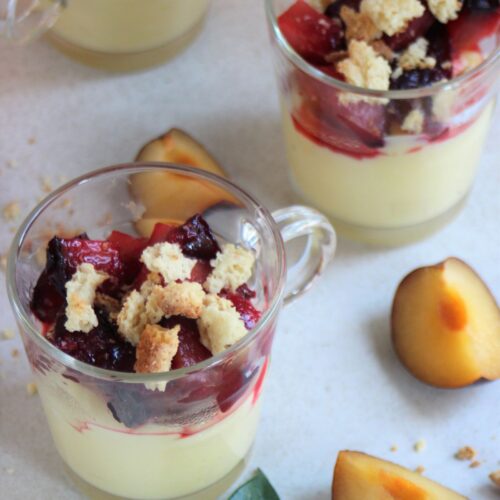 Glass jars with cream, plum compote, and crumbs. Slices of plums on the side.