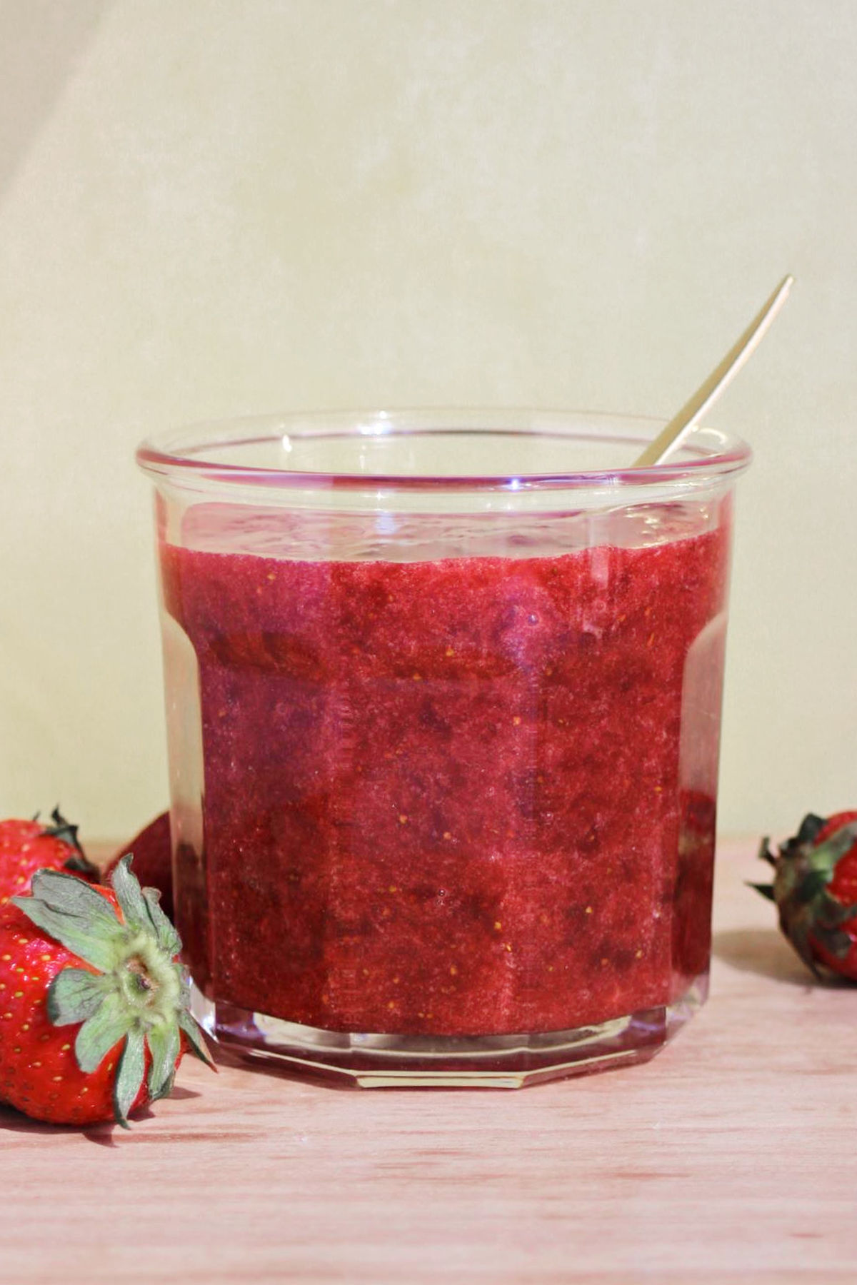 Glass with strawberry jam. Beige background, light wooden surface.