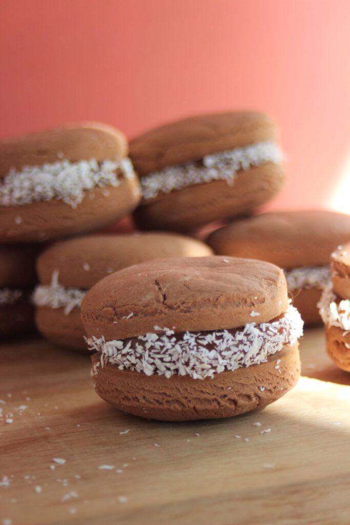 Chocolate alfajor with dulce de leche on a wooden surface. More chocolate alfajores behind.
