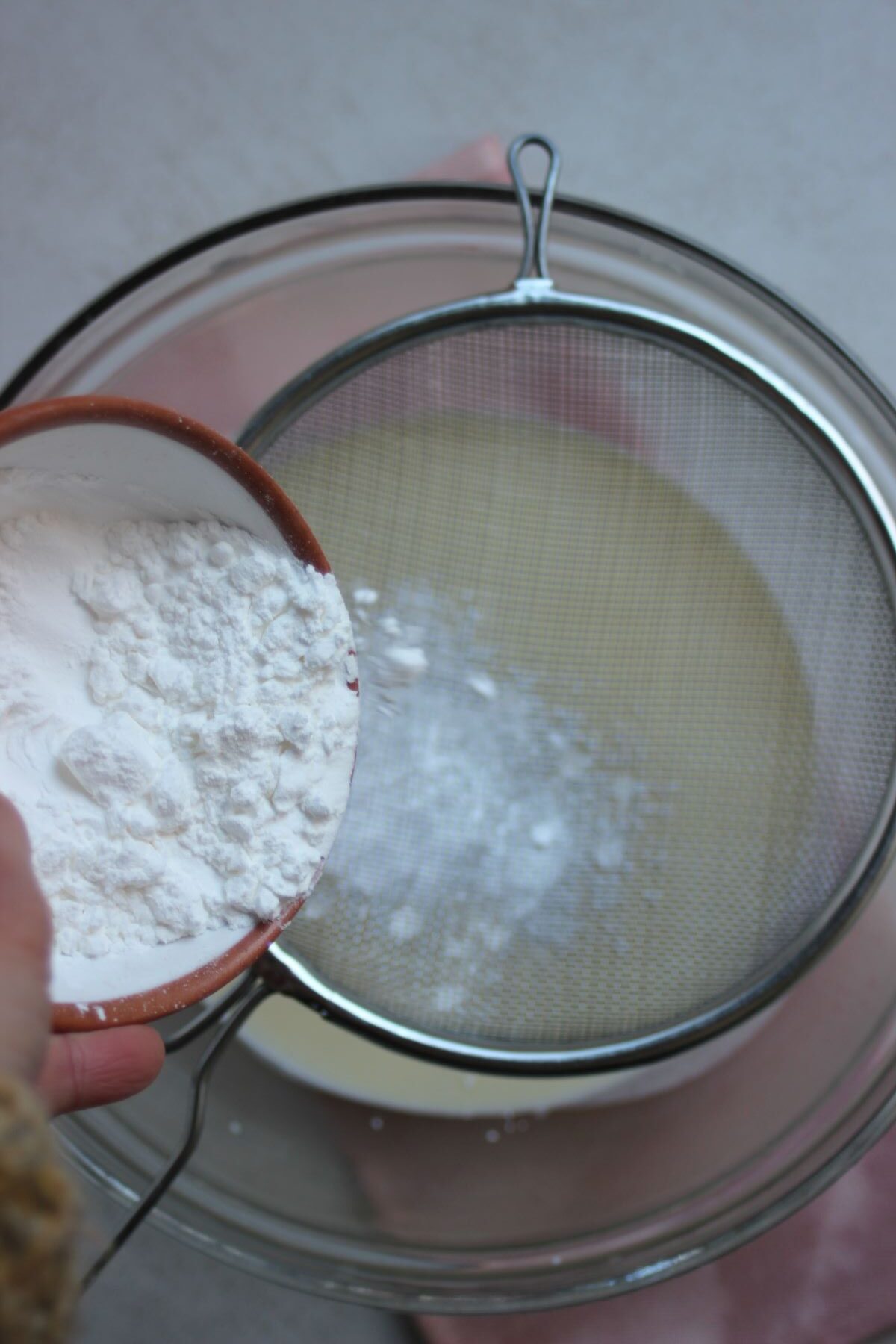 A plate with corn starch is being sieve into a glass bowl.