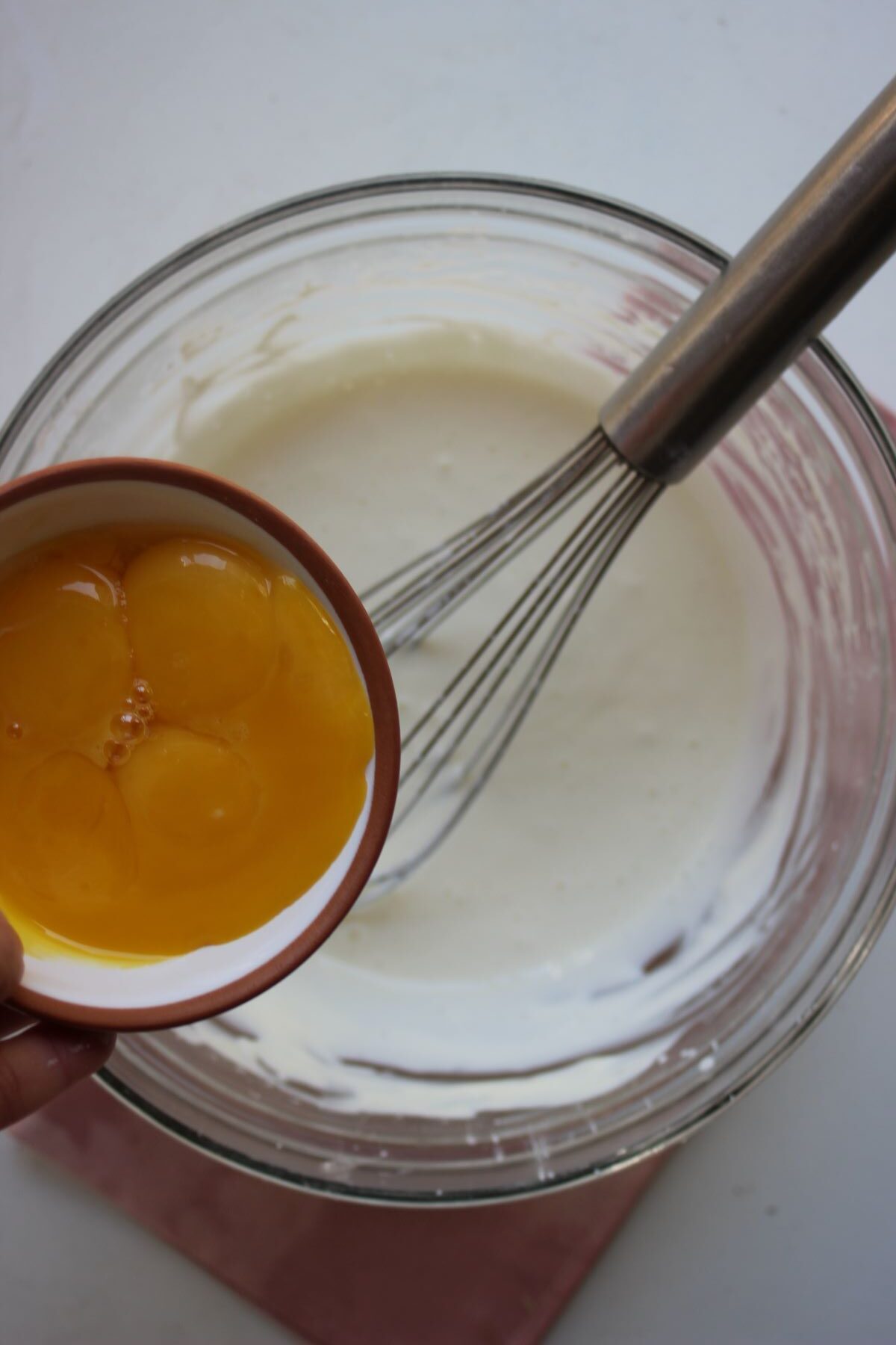 Plate with egg yolks is about to be poured into glass bowl with a white mixture.