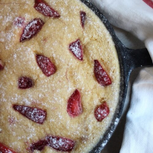 Strawberry clafoutis in a black skillet and a white napkin seen from above.