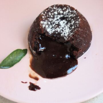 Molten lava cake and melted chocolate coming out of it on a pink plate.