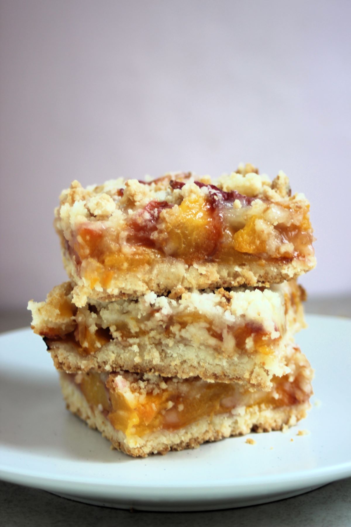 Three peach crumb bars stacked on a white plate.