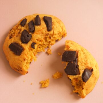Broken pumpkin cookie with chocolate chunks on a pink surface.
