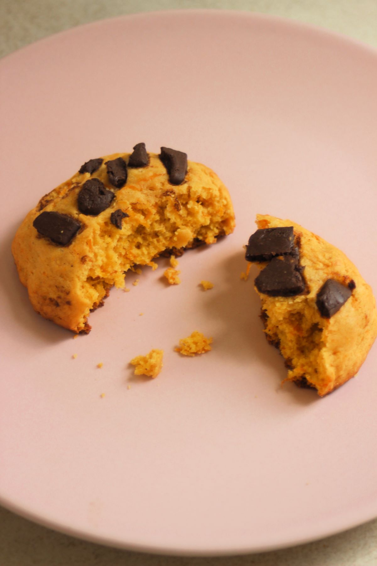 Broken pumpkin cookie with chocolate chunks on a pink plate.