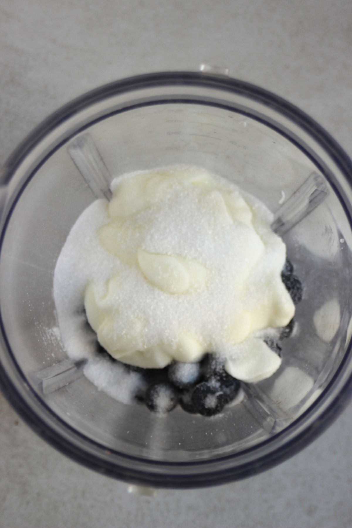 Blender with blueberries, sugar, and yogurt seen from above.