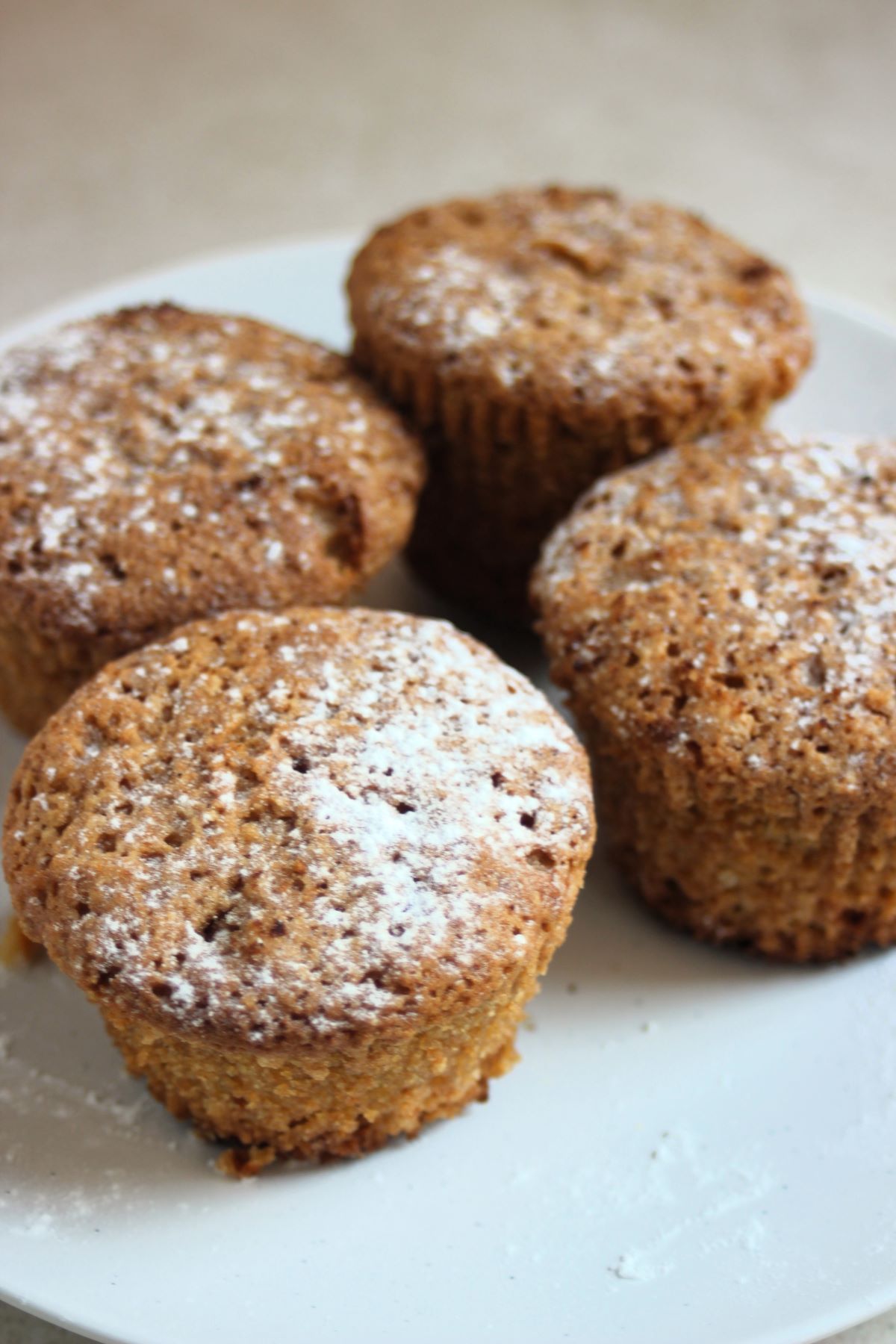 Four muffins with powdered sugar on a white plate.