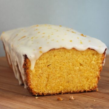 A piece of orange loaf cake with icing on a wooden board.