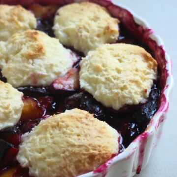 Round baking pan with plum cobbler on a white surface.