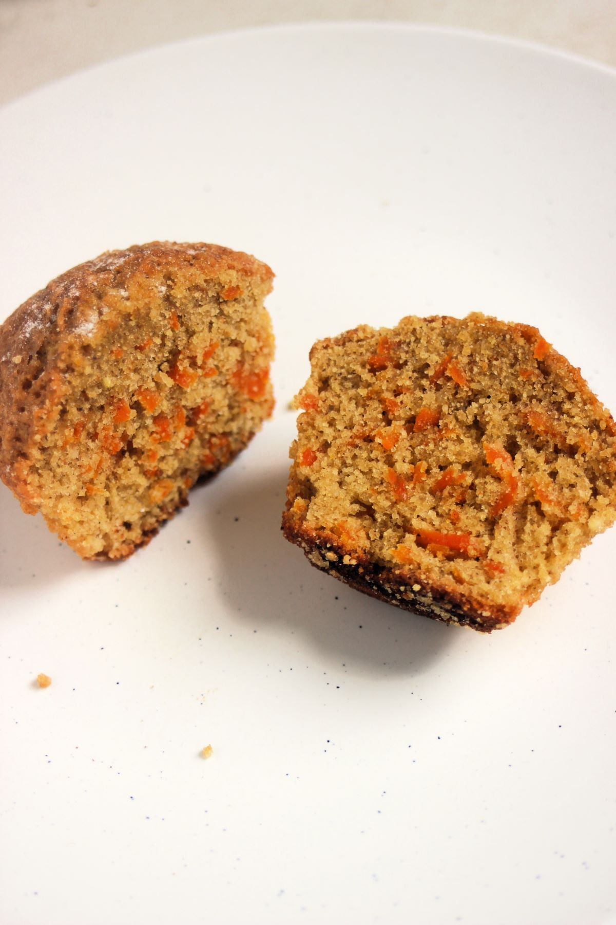 A carrot cake muffin cut in two on a white plate.