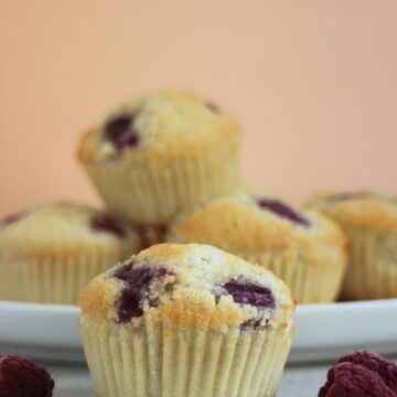 Raspberry muffin and raspberries on the sides. More muffins behind on a white plate.