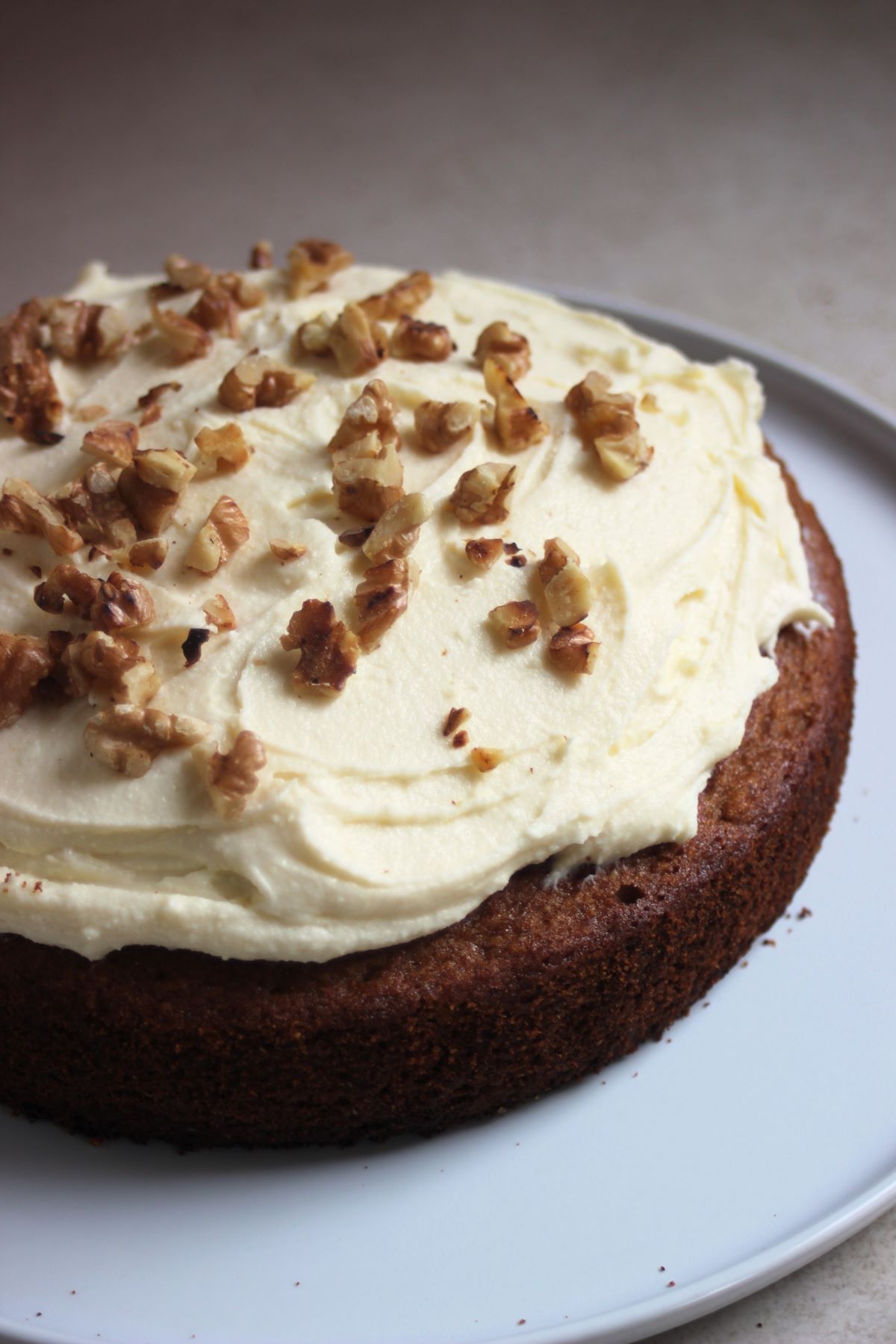 Sweet potato cake with cream cheese frosting and chopped nuts on a white plate.