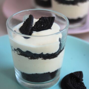 Glass with lemon mousse and Oreos on a light blue plate. Broken Oreos on the side.