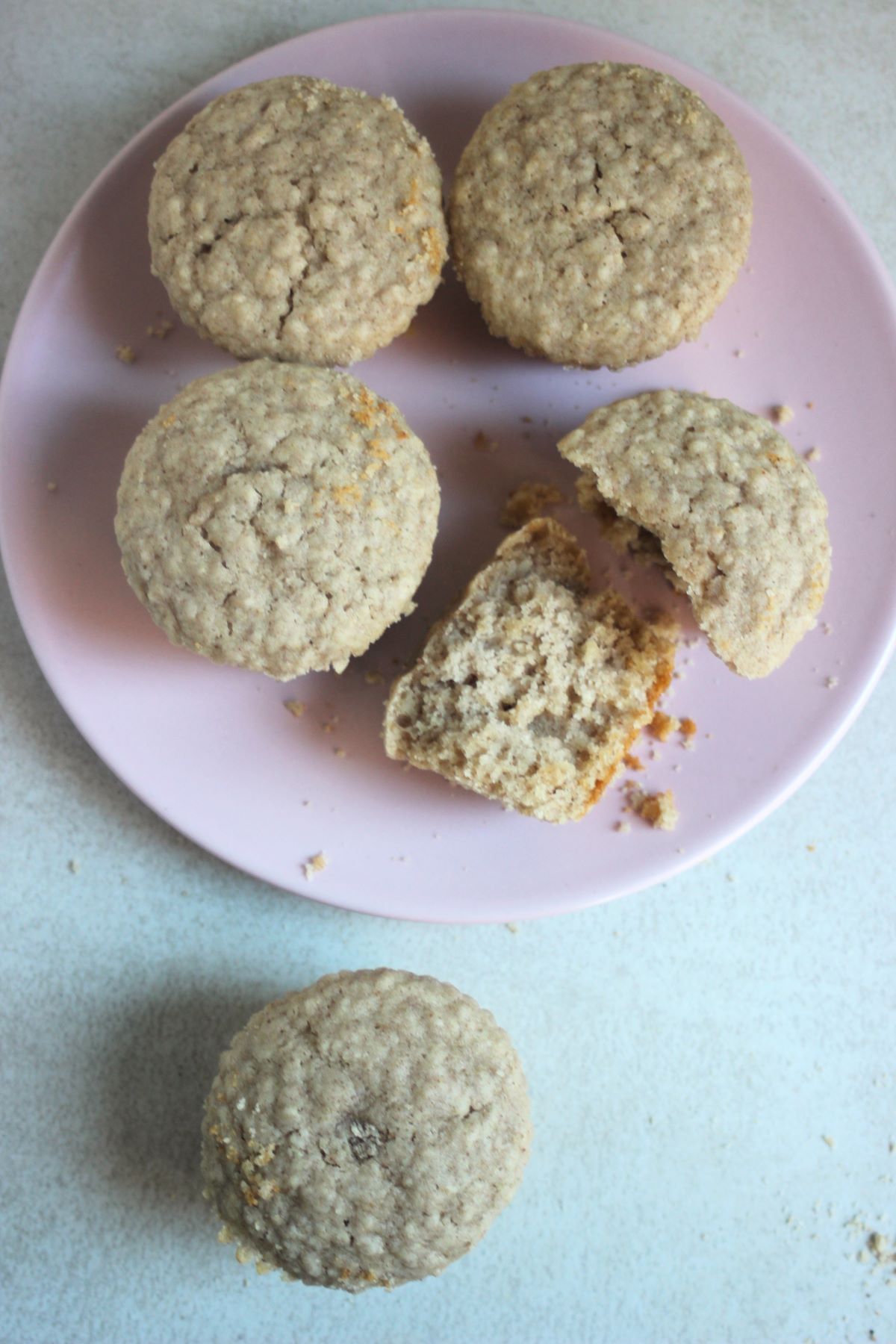 Oatmeal muffins on a pink plate seen from above. One muffin beside the plate.