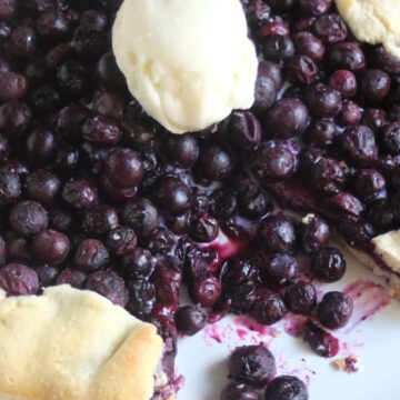 Blueberry galette without a piece and a scoop of ice cream on a white plate.