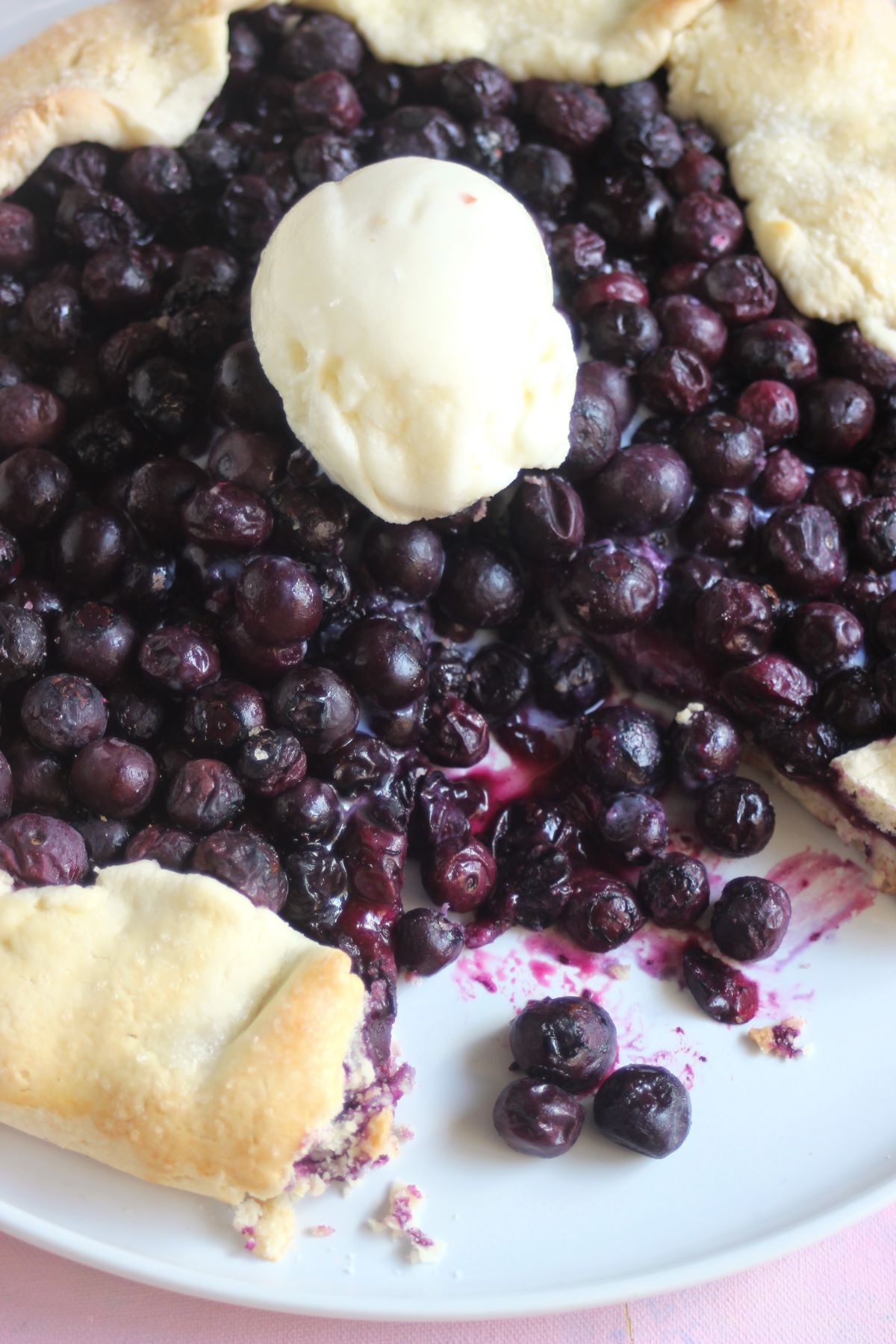 Blueberry galette without a piece and a scoop of ice cream on a white plate.