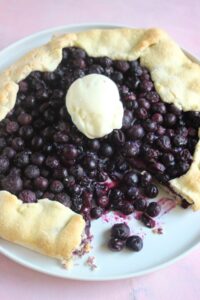 Blueberry galette without a piece and a scoop of ice cream on a white plate.