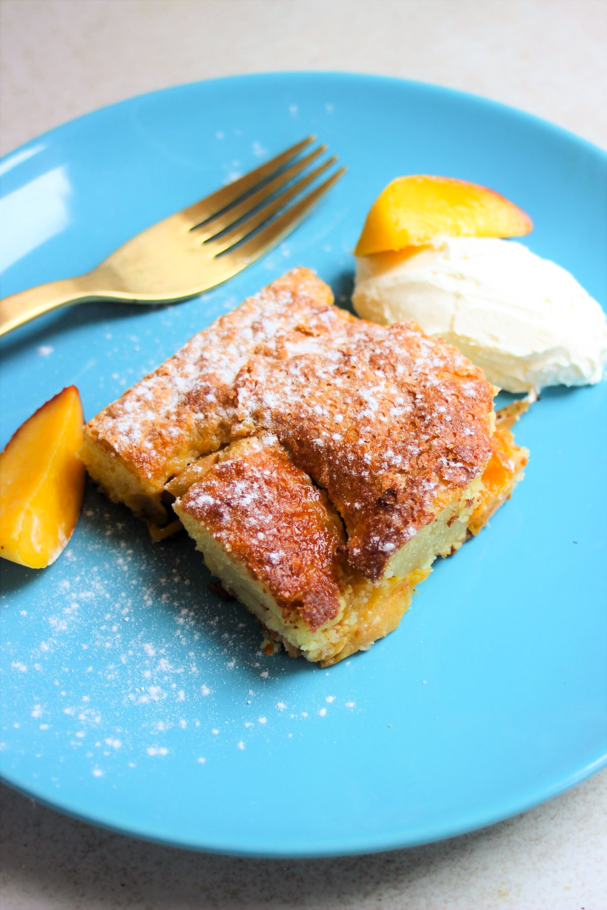 A portion of peach cake with whipped cream and peach slices on a turquoise plate.