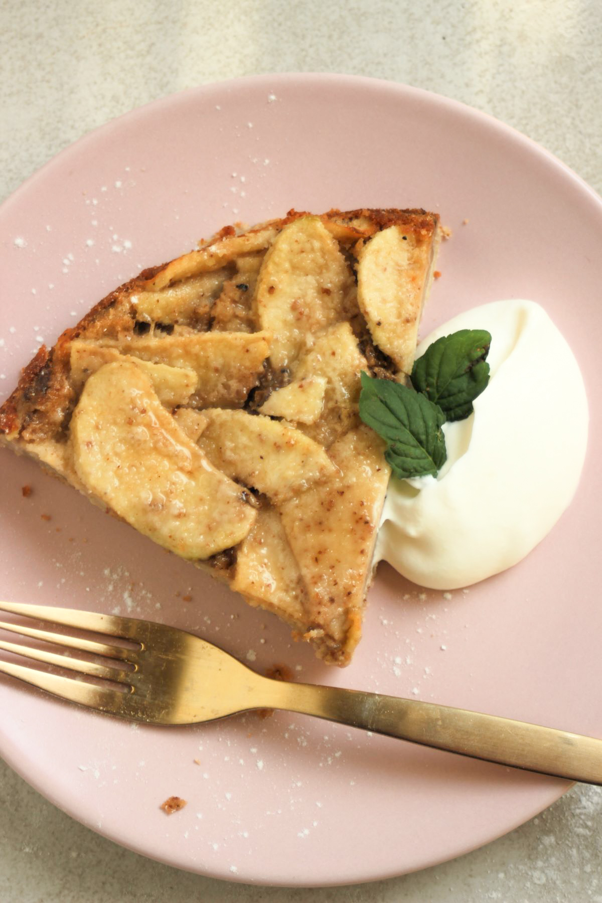 Portion of apple cake with whipped cream on a pink plate.