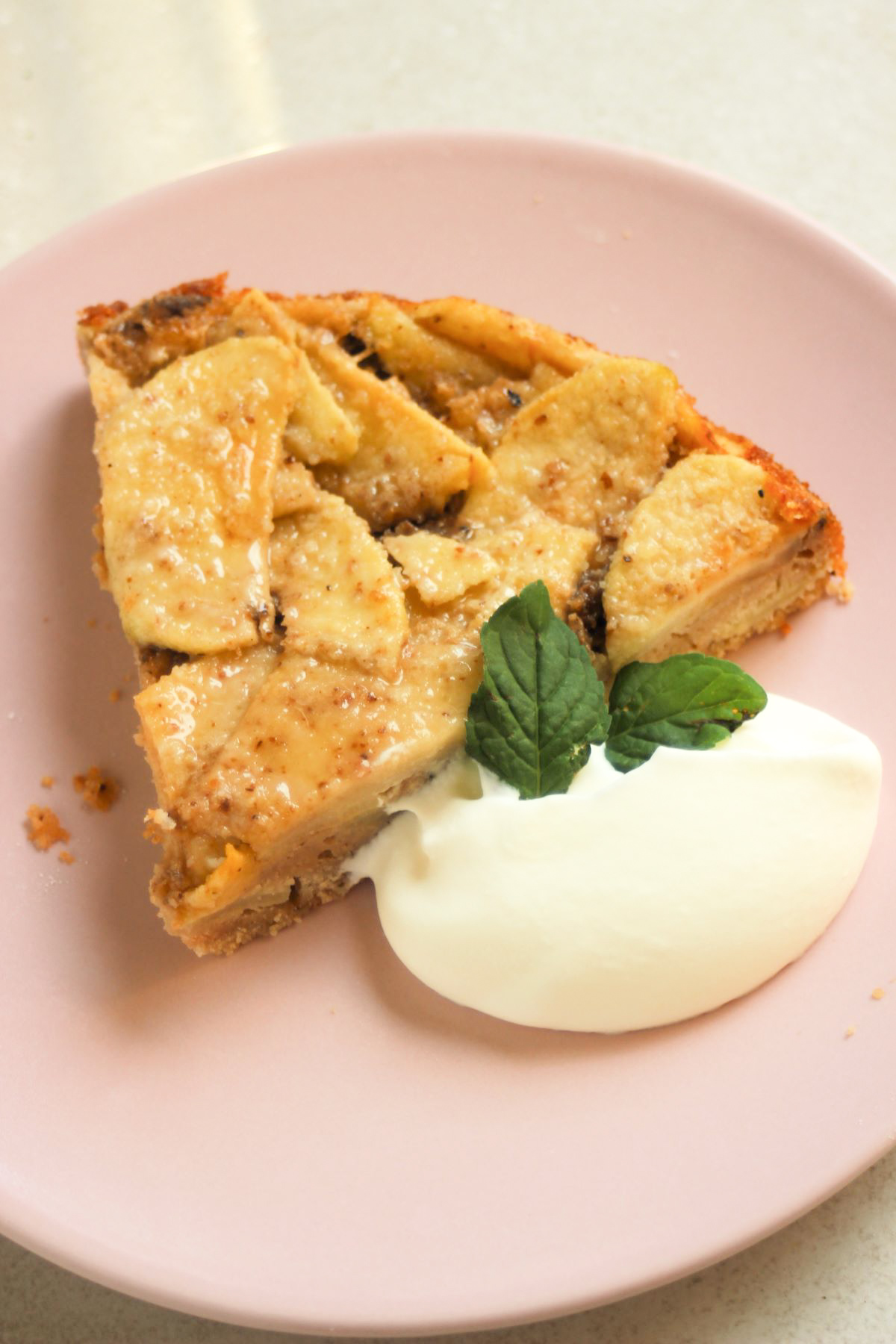 Portion of apple cake with whipped cream on a pink plate.