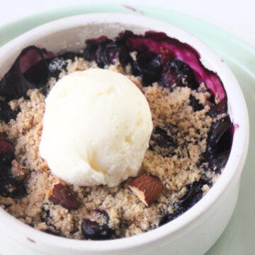 Blueberry crisp and a scoop od ice cream in a small round white bowl on a aqua green plate.