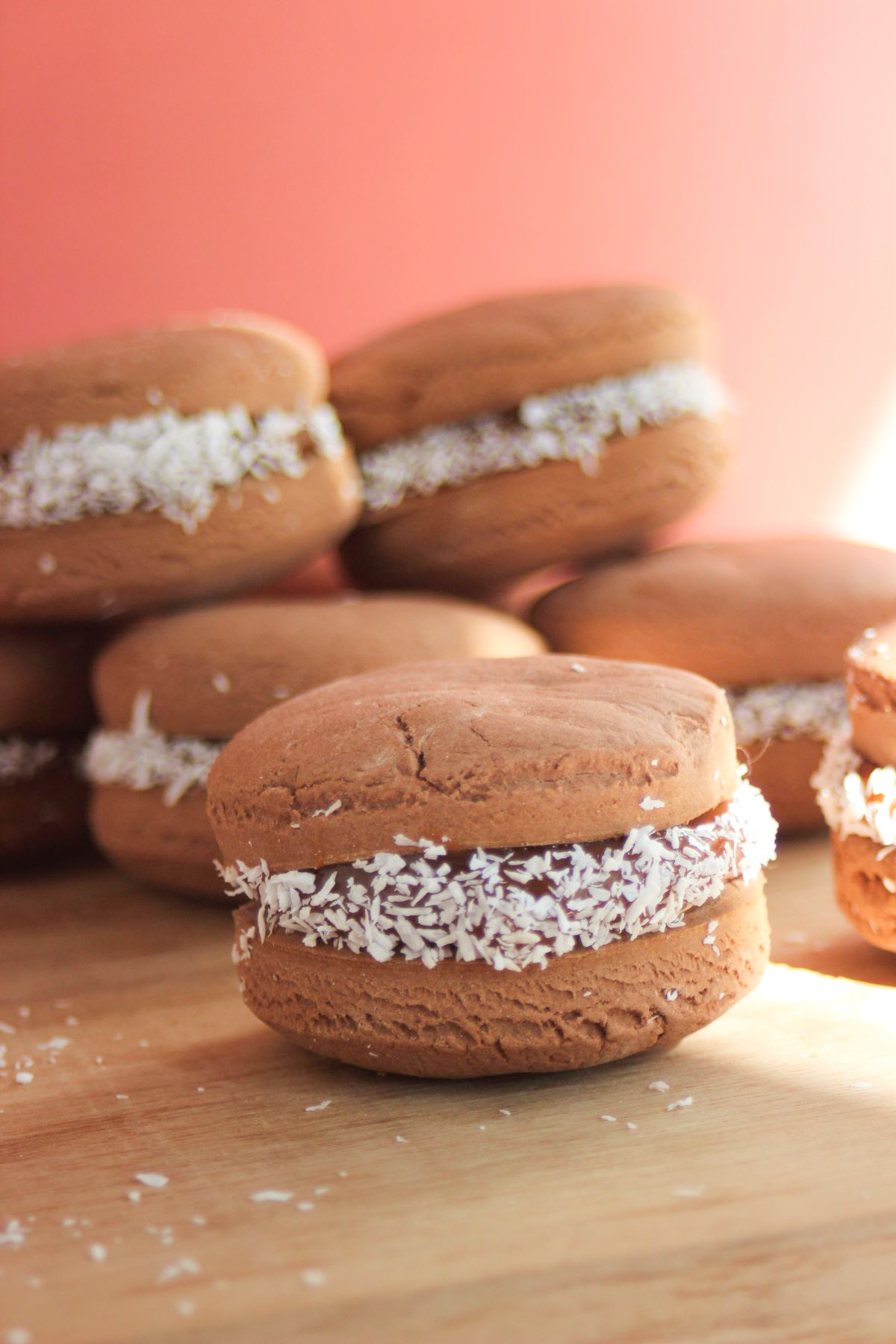 Chocolate alfajor with dulce de leche on a wooden surface. More chocolate alfajores behind.