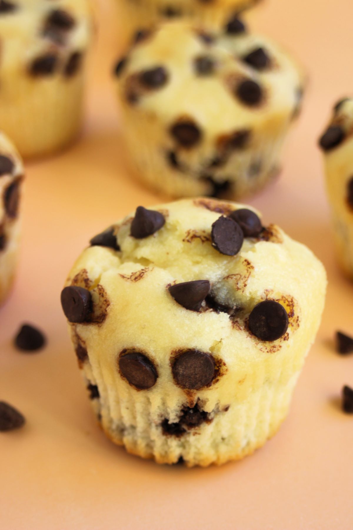 Chocolate chip muffins on a light orange surface,