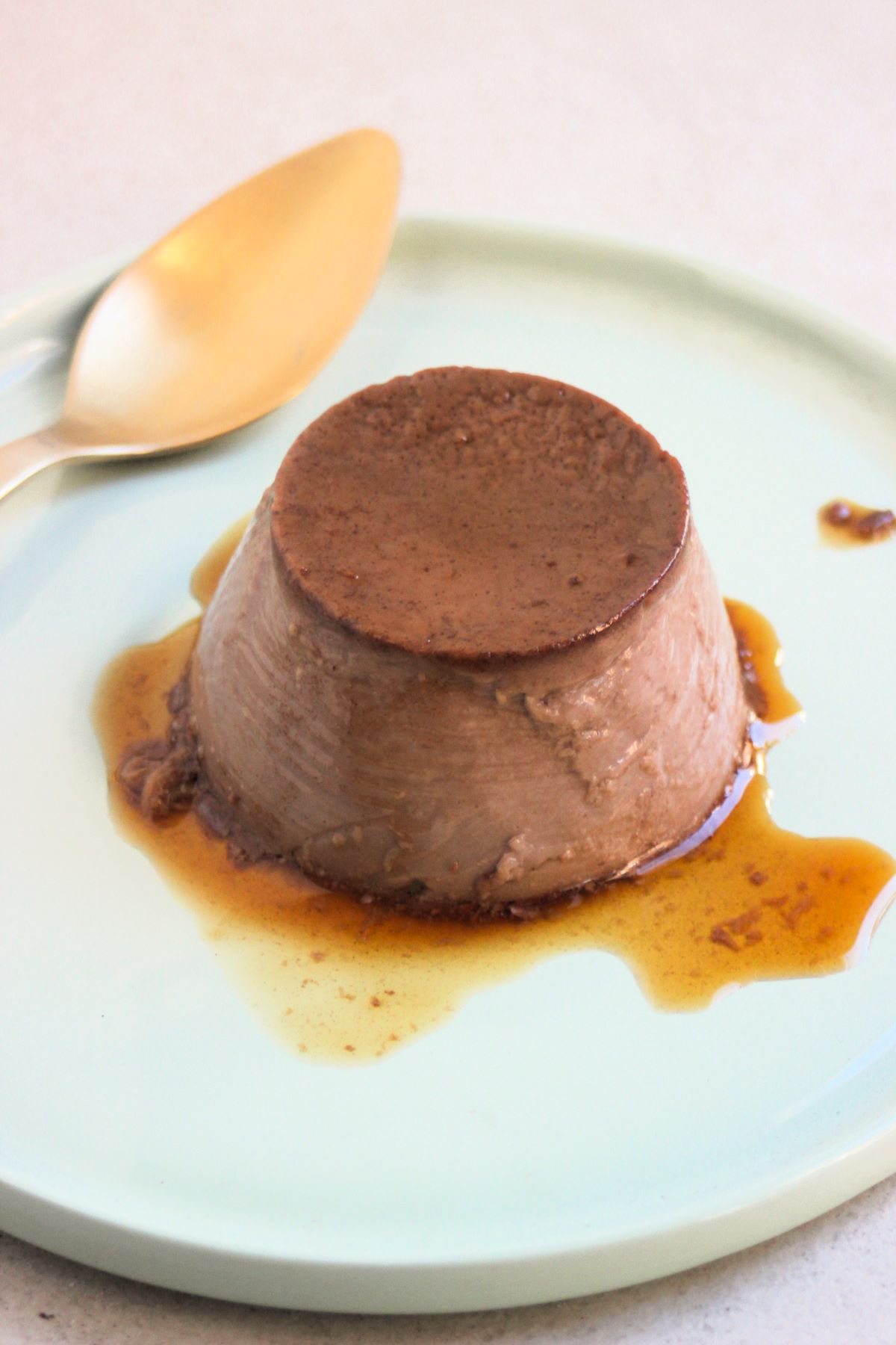 Chocolate flan with caramel on an aqua-green plate and a golden fork.