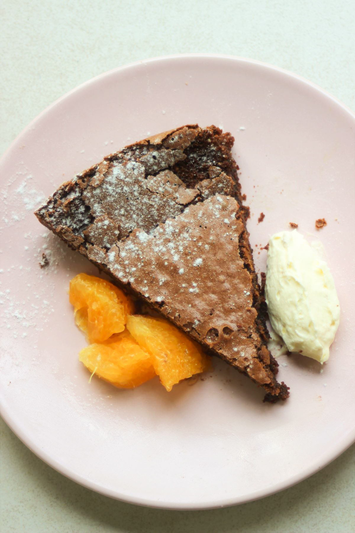 Portion of chocolate cake with orange slices and whipped cream on a pink plate.