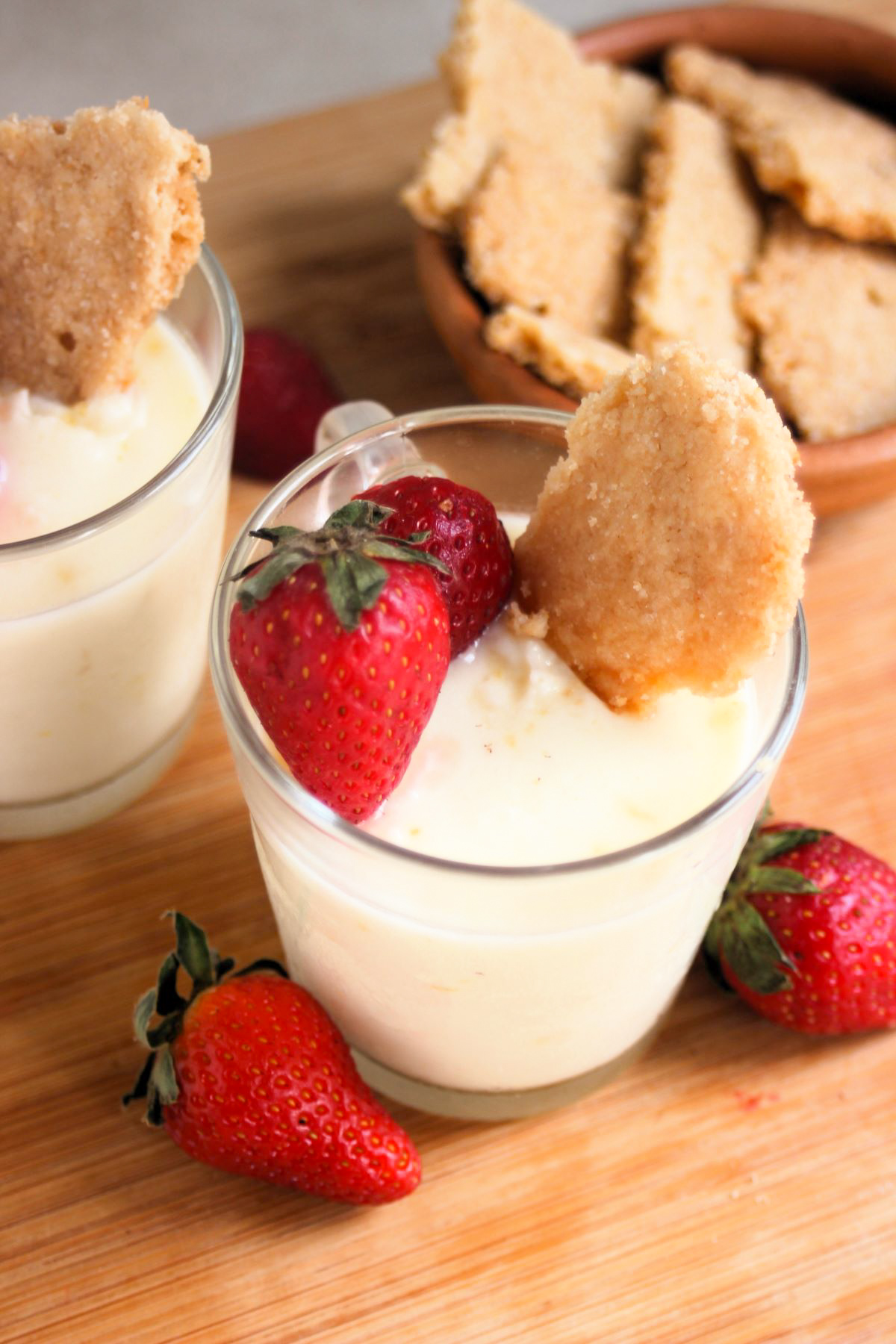 Glass cup with lemon posset, strawberries, and shortcake cookie seen from above Strawberries on the side.