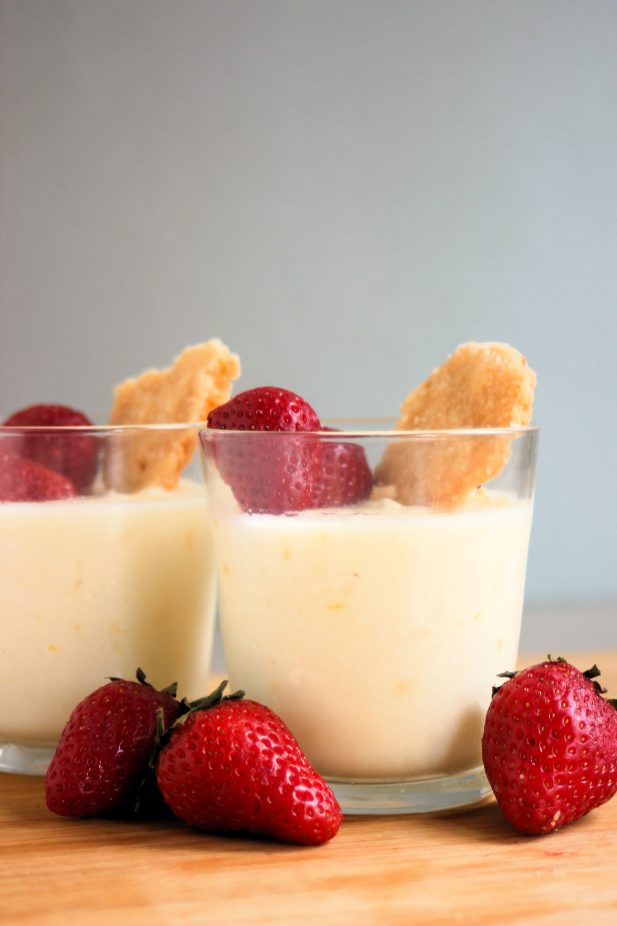 Glass cup with lemon posset, strawberries, and shortcake cookie. Strawberries on the side.