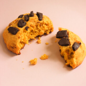 Broken pumpkin cookie with chocolate chunks on a pink plate.