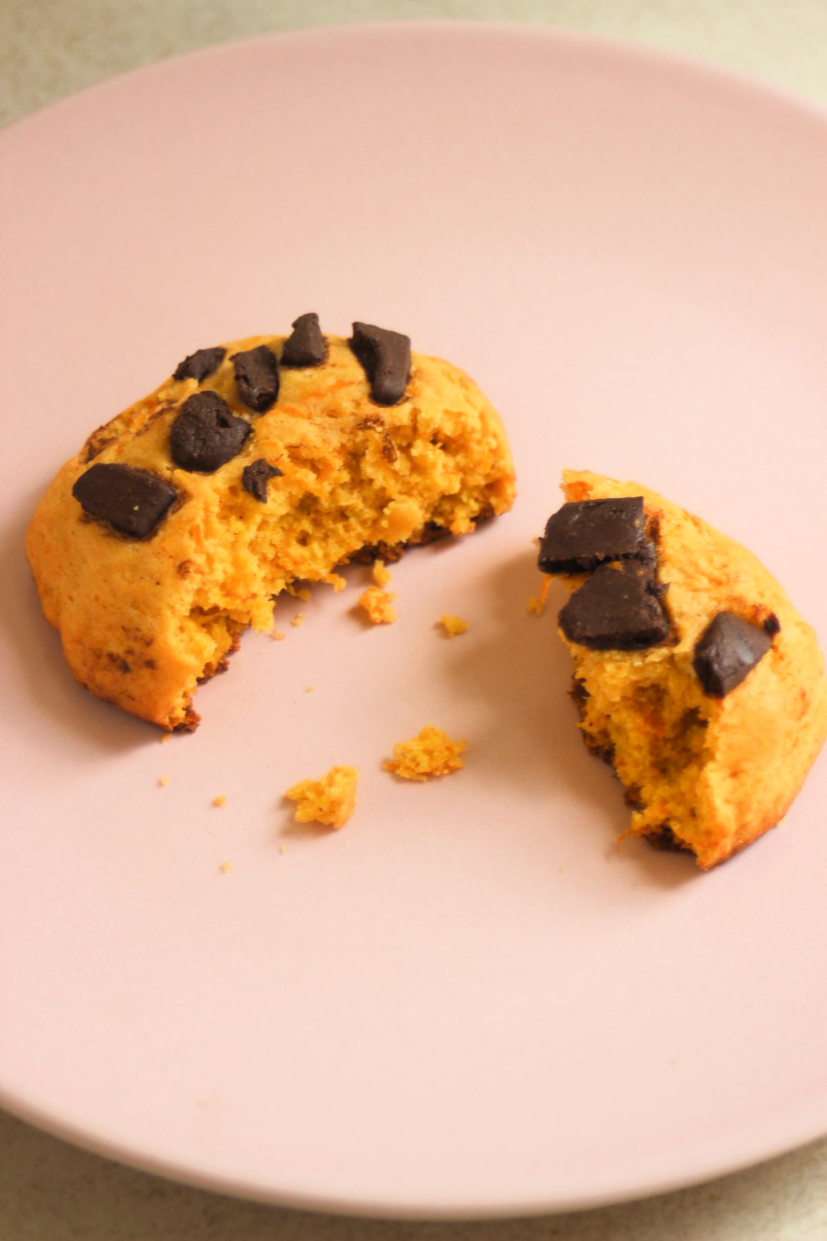 Broken pumpkin cookie with chocolate chunks on a pink plate.