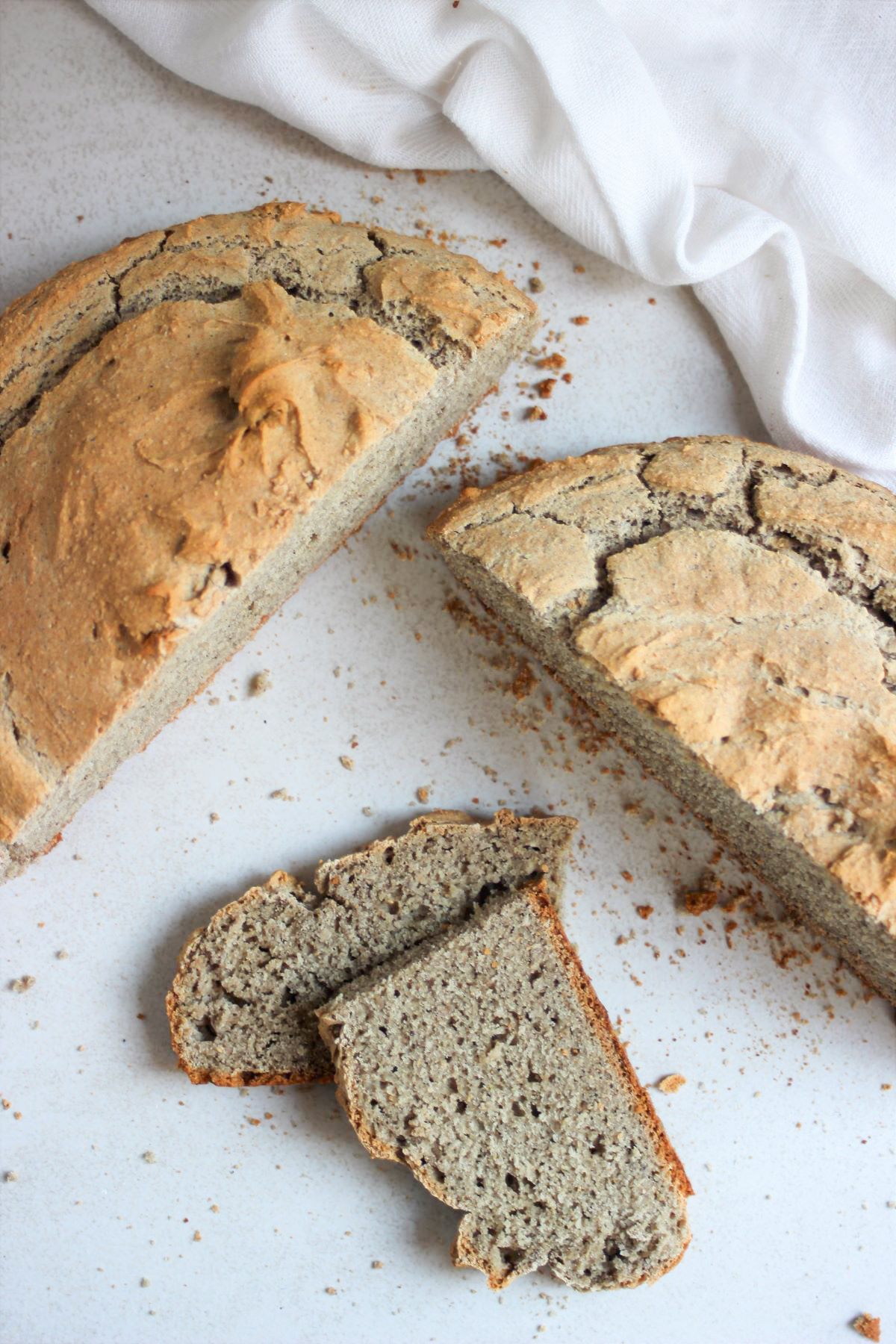 Soda bread cut in two halves and a slice cut in two on a white surface seen from above.