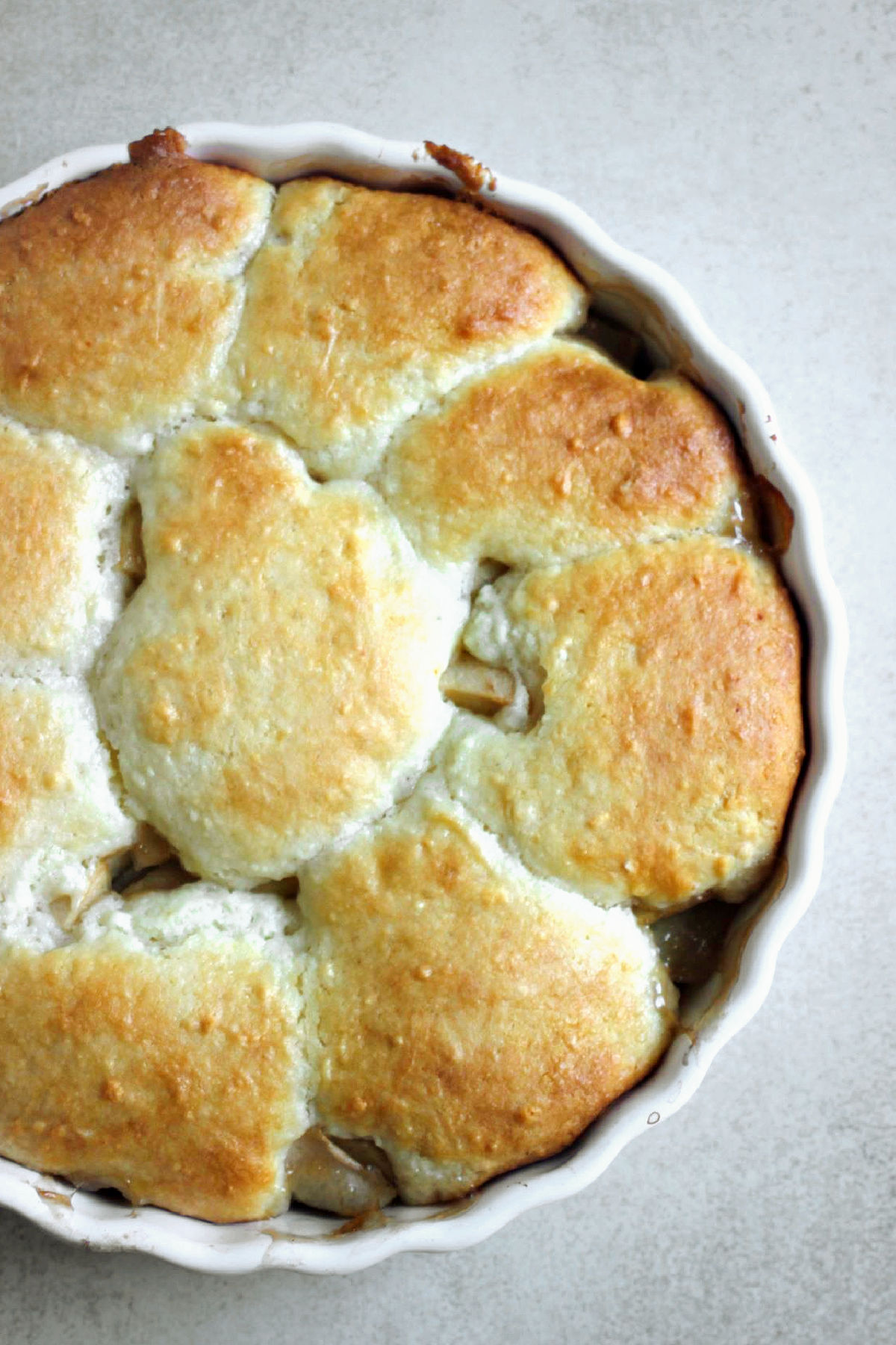 Apple cobbler in a round white baking didh on a white surface seen from above.