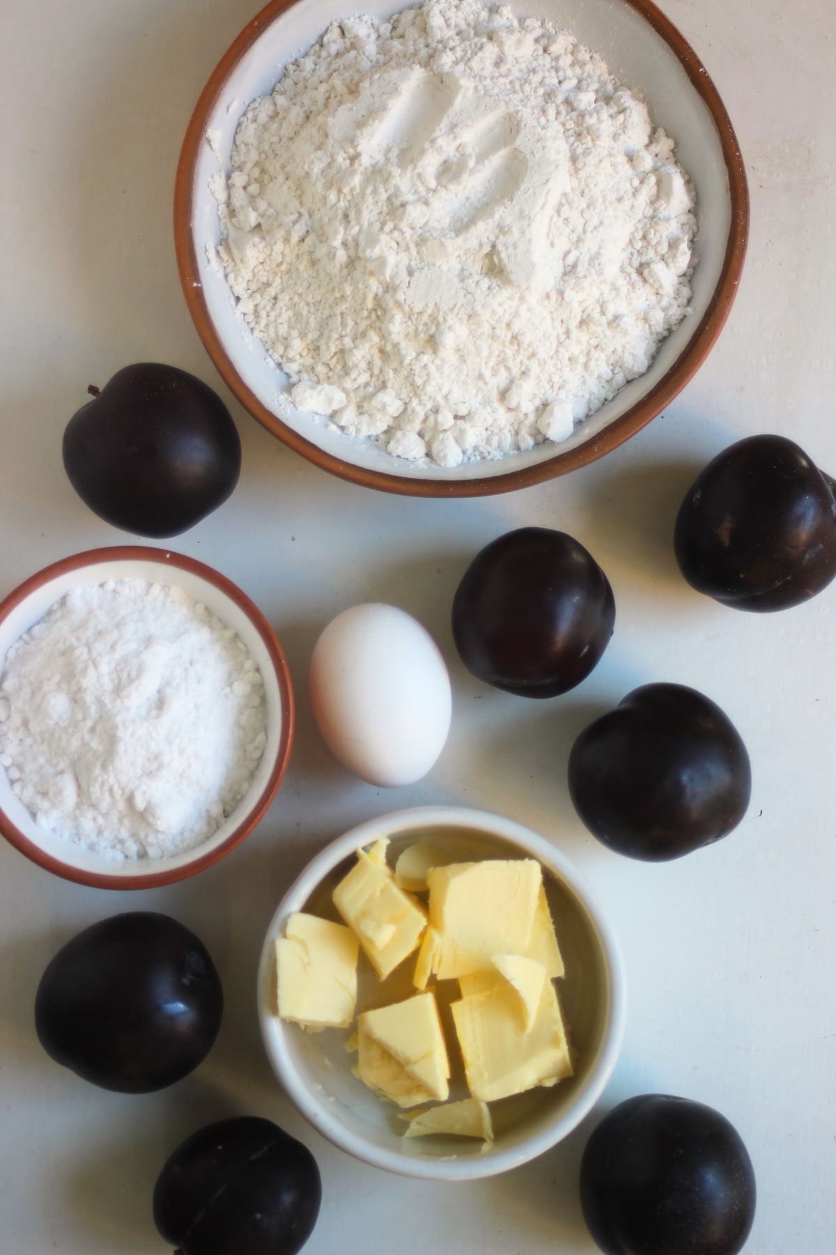 Plum tart ingredients on a white surface seen from above.